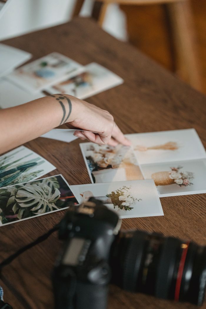 gallery-1 Crop unrecognizable photographer pointing at printed photos scattered on wooden table near professional photo camera