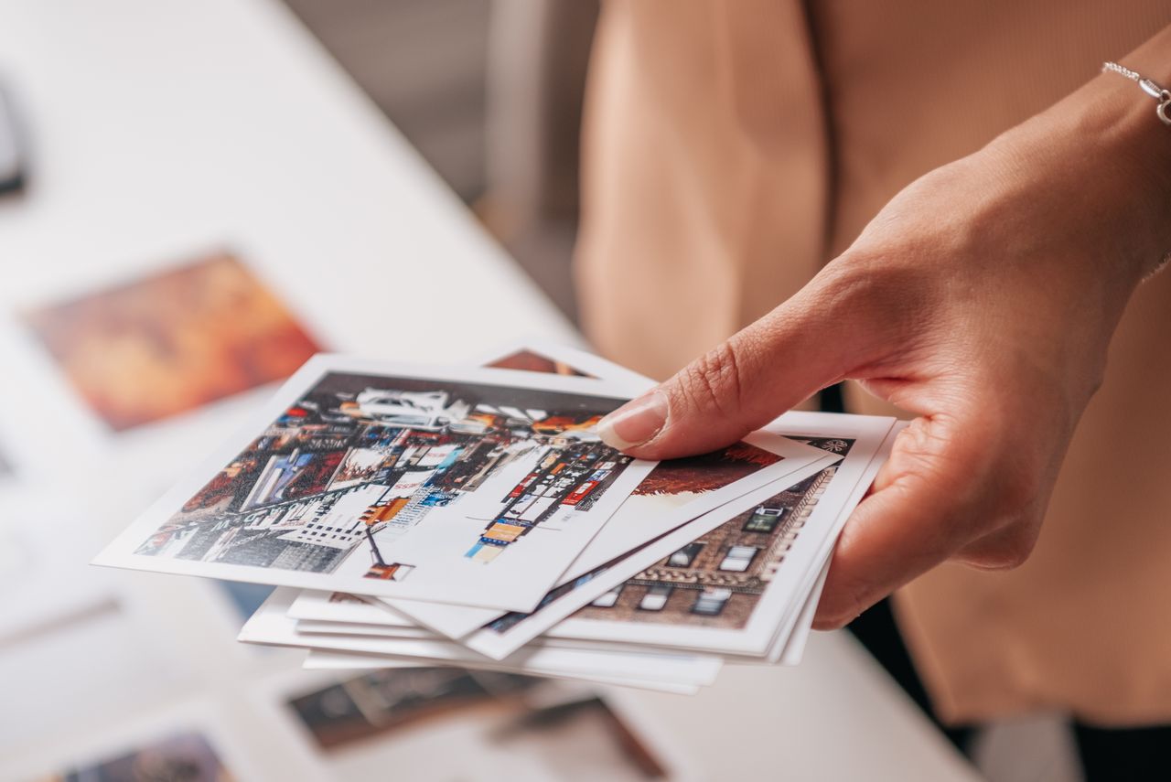 services-02 A hand holding printed photographs featuring urban cityscapes on a white table.